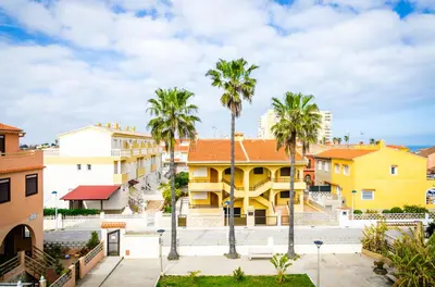 a row of palm trees in front of a yellow building at Casa En La Playa Del Rey in Mareny Barraquetas