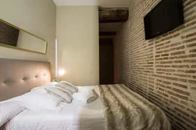 a bedroom with a white bed with a brick wall at Cosy Rooms Bolsería in Valencia