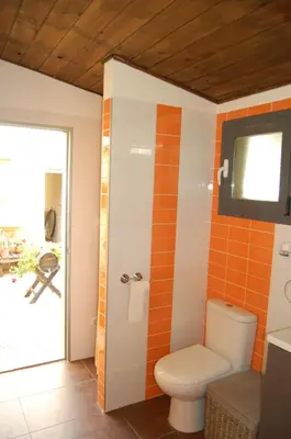 a bathroom with a toilet and an orange tile wall at Casa Tambor in Puebla de Vallbona