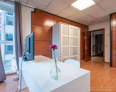 a desk with a computer and a vase with a flower on it at Suites Rooms Valencia in Valencia