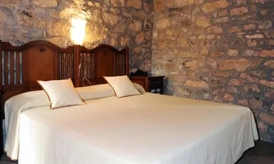 a bedroom with a white bed in a stone wall at Hotel Restaurant Verdià in Sueras