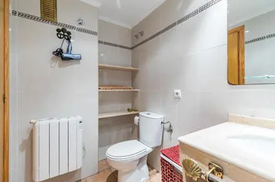 a white bathroom with a toilet and a sink at Beach Apartment with beautiful view in Port Saplaya