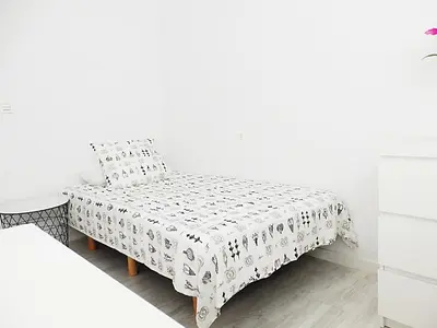 a white bedroom with a bed and a table at Campanar Flat in Valencia