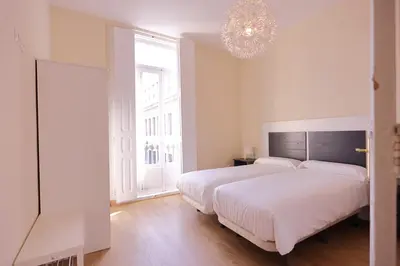 a white bedroom with a large bed and a chandelier at Apartamentos Dormavalencia in Valencia