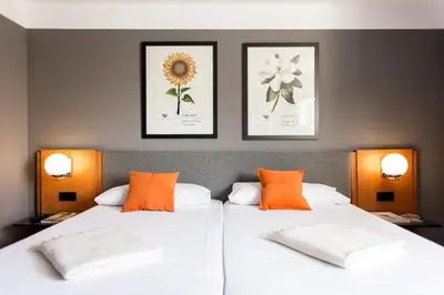 a bedroom with two beds with orange pillows and pictures on the wall at Hotel Malcom and Barret in Valencia