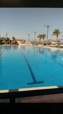 a large swimming pool with blue water and palm trees at Sea view Port Saplaya Apartments,2 in Port Saplaya