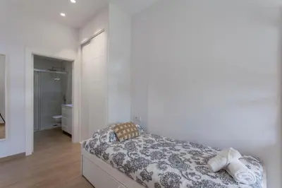a white bedroom with a bed and a bathroom at ApartUP Patacona Select in Valencia