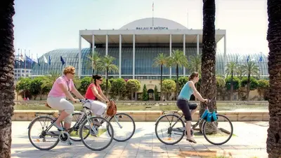 three women riding bikes in front of a building at SH Suite Palace in Valencia