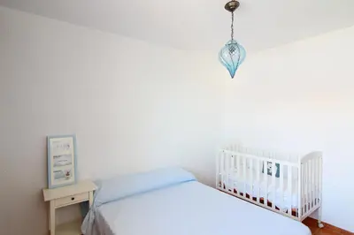 a white bedroom with a crib and a chandelier at Global Vacacional, Adosado en la playa con piscina in Sagunto