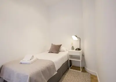 a white bedroom with a bed and a night stand at Apartamentos San Vicente in Valencia