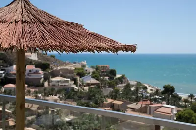 a straw umbrella on a balcony with the ocean at Big Terrace Apartment Cullera in Cullera