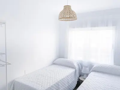 a white bedroom with two beds and a chandelier at NUEVO, a 70 metros de la playa y con vistas al mar in Cullera