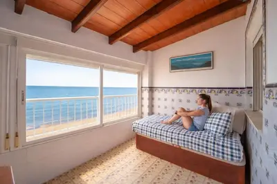 a woman sitting on a bed in a room with a window at Apartamento en primera línea de playa con vistas al mar in Mareny Barraquetas