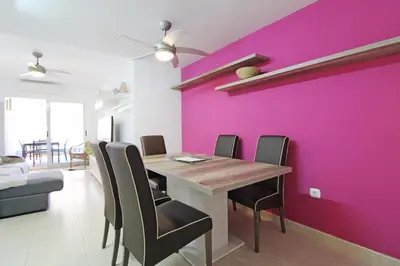 a dining room with a pink wall and a table and chairs at Global Vacacional, Apartamento en la playa de Canet d'en Berenguer in Canet de Berenguer