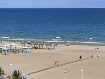 a beach with people walking on the sand and the ocean at 1ere soleil levant in Puerto de Sagunto