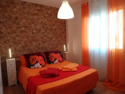 a bedroom with a bed with orange sheets and a brick wall at LAS PALOMAS, appartement 2 chambres avec piscine in Turís