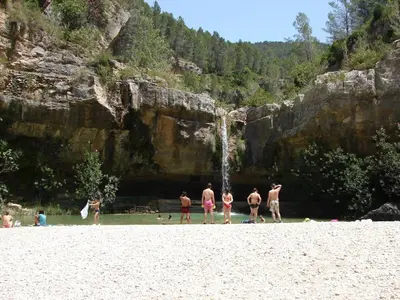 a group of people standing on a beach with a waterfall at La Gata Mala in Navarrés