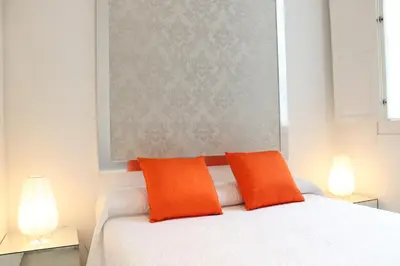 two orange pillows on a white bed with two lamps at Apartamento Reina Catedral in Valencia