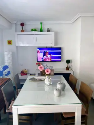 a dining room with a white table and a tv at Apto POSEIDON CON PARKING EN EDIFICIO SUBTERRANEO in Cullera
