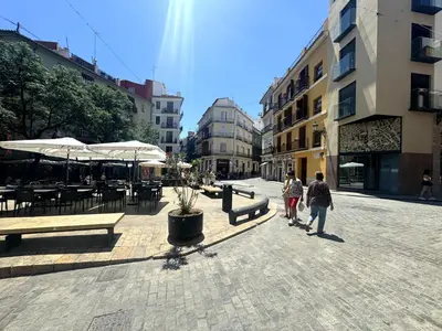 two people walking down a street with benches and umbrellas at Precioso Apartamento en la Plaza del Tossal in Valencia