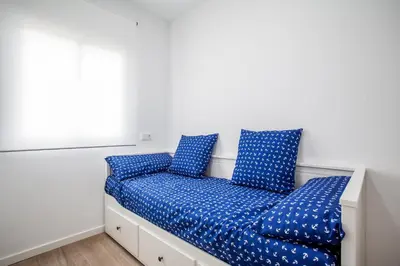a bed with blue pillows in a white room at Ático con espectacular terraza y vistas al mar in El Perelló
