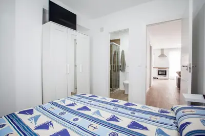 a white bedroom with a blue and white bed at Ático con espectacular terraza y vistas al mar in El Perelló