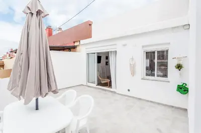 a patio with a white umbrella and a table and chairs at Ático con espectacular terraza y vistas al mar in El Perelló