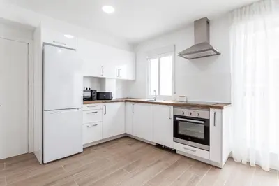a white kitchen with white cabinets and a stove at Ático con espectacular terraza y vistas al mar in El Perelló