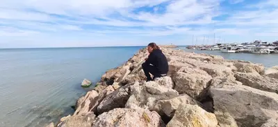 a woman sitting on the rocks by the water at Cozy Apartment close to the beach in beatiful area in El Perelló