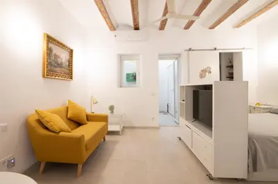 a white bedroom with a yellow chair and a bed at Cabanyal old fisherman's house in Valencia