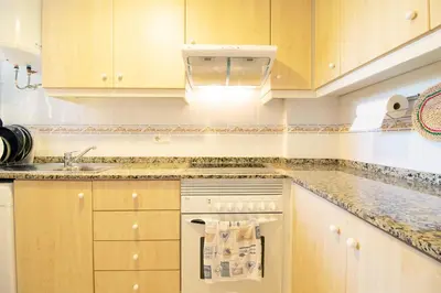 a kitchen with wooden cabinets and a sink at Global Vacacional, Practico apartamento con piscina en Residencial Brezo Canet in Canet de Berenguer