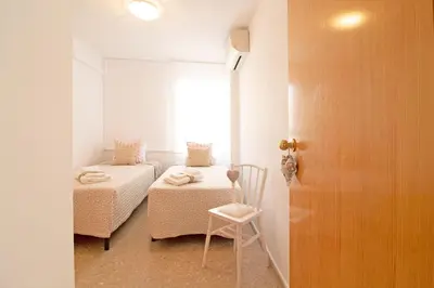 a room with two beds and a chair and a window at Global Vacacional, Practico apartamento con piscina en Residencial Brezo Canet in Canet de Berenguer