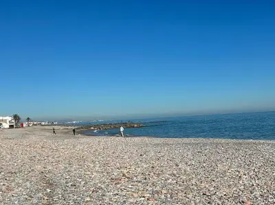 a rocky beach with people walking on the water at Precioso apartamento con piscina en Moncofar in Moncófar