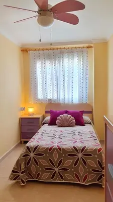 a bedroom with a bed with purple pillows and a ceiling fan at Piso familiar con amplia terraza 300m de la playa in Cullera