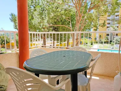 a green table and chairs on a balcony with a pool at Global Vacacional, Apartamento con piscina en Residencial Brezo in Canet de Berenguer