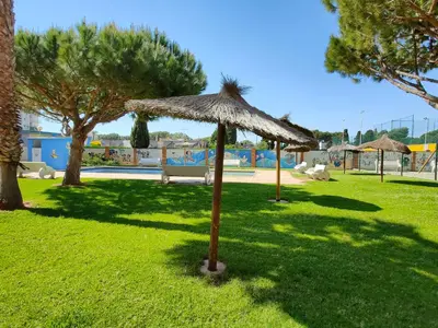 a grass umbrella in a park with a pool at Global Vacacional, Apartamento con piscina en Residencial Brezo in Canet de Berenguer