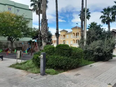 a playground in front of a yellow building with palm trees at Relax Les Palmeres in Sueca
