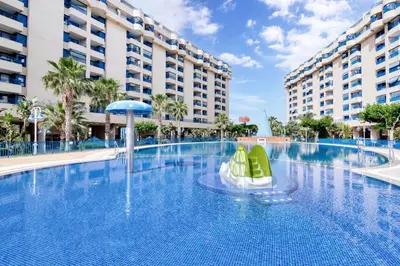 a large swimming pool with green chairs and buildings at Ático frente al mar, PataconaBlue, complejo vacacional in Valencia