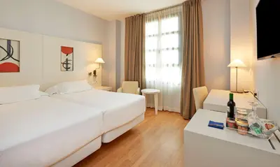 a hotel room with a bed and a table with a bottle of wine at NH Valencia Las Artes in Valencia
