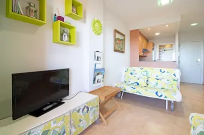 a living room with a flat screen tv and a chair at Global Vacacional, Apartamento con gran terraza y piscina in Canet de Berenguer