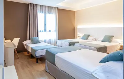 a hotel room with three beds and a window at Hotel Olympia Valencia in Alboraya