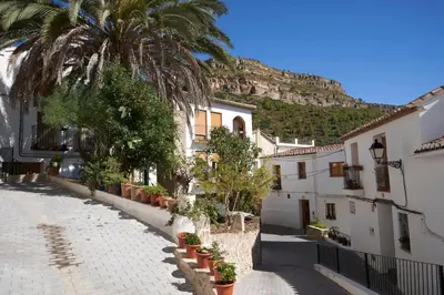 a street with buildings and palm trees and a mountain at El mas allà in Chulilla