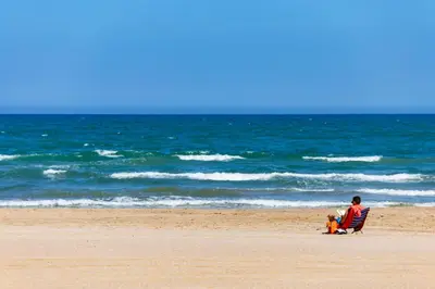 a man and a child sitting in a chair on the beach at Florazar Apartment Cullera Beachfront in Cullera