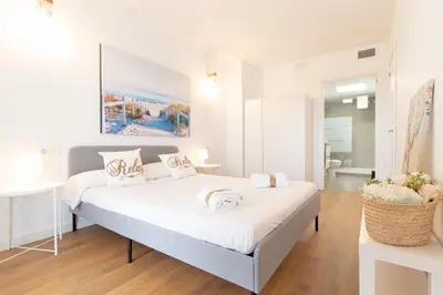 a white bedroom with a large white bed and a bathroom at Global Vacacional, Moderno apartamento en Canet al Mar in Canet de Berenguer