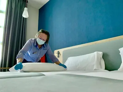 a woman in a mask making a bed at Holiday Inn Express Ciudad de las Ciencias by IHG in Valencia