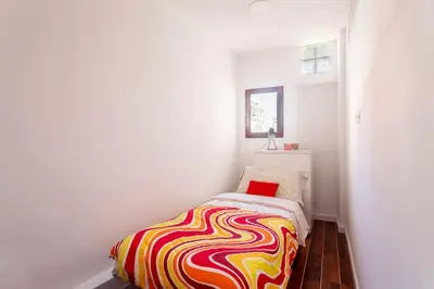 a small white room with a bed with a colorful blanket at 7P céntrico piso con encanto in Valencia