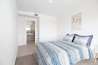 a white bedroom with a bed with blue and white sheets at Global Vacacional, Apartamento con terraza y vistas a la piscina en Gran Canet in Canet de Berenguer