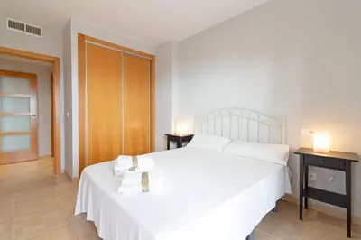 a bedroom with a white bed and two night stands at Global Vacacional, Apartamento con terraza y piscina en la playa de Canet in Canet de Berenguer