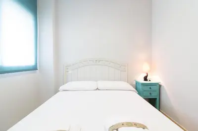 a bedroom with a white bed and a blue nightstand at Global Vacacional, Apartamento con terraza y piscina en la playa de Canet in Canet de Berenguer