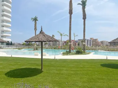 a resort with a pool and a umbrella in the grass at Moderno apartamento con vistas a la costa mediterranea en Gran Canet in Canet de Berenguer